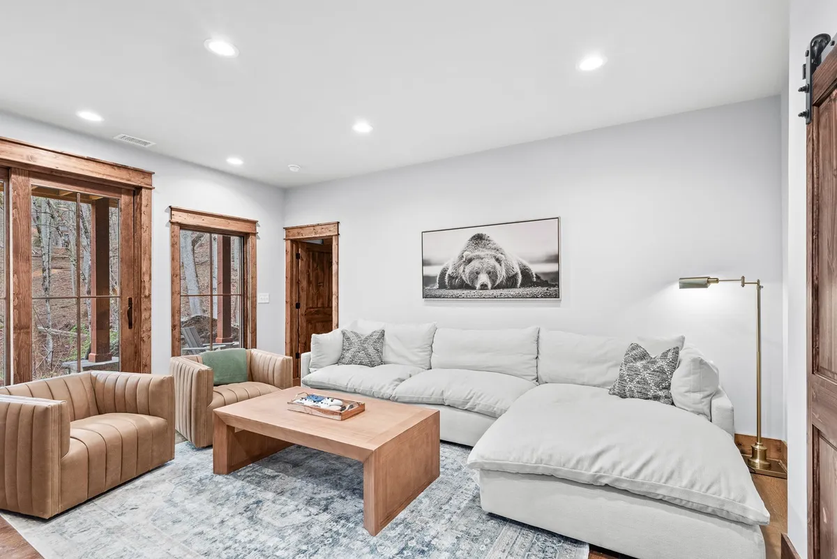 A different angle of a den or living area with a large sectional sofa, wooden coffee table, and comfortable armchairs. Bear-themed artwork adds a playful, rustic lodge touch. The room is designed for relaxation with plenty of seating, all arranged to encourage conversation or movie watching.