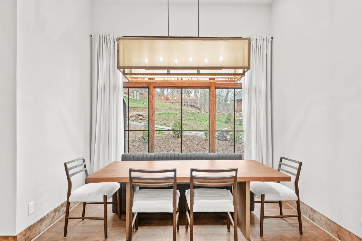 A dedicated dining area with a welcoming wooden table, chandelier overhead, and a window offering tranquil views. The arrangement is ideal for shared meals, lively game nights, or lingering conversations, all bathed in soft, natural light.