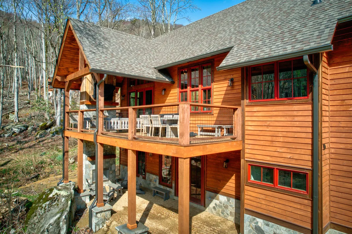 The image shows a wooden balcony with red window frames and a sturdy stone base. The balcony offers ample space for relaxing outdoors, with a view that hints at the surrounding mountains and greenery—an ideal place for guests and their dogs to unwind and enjoy the fresh air together.