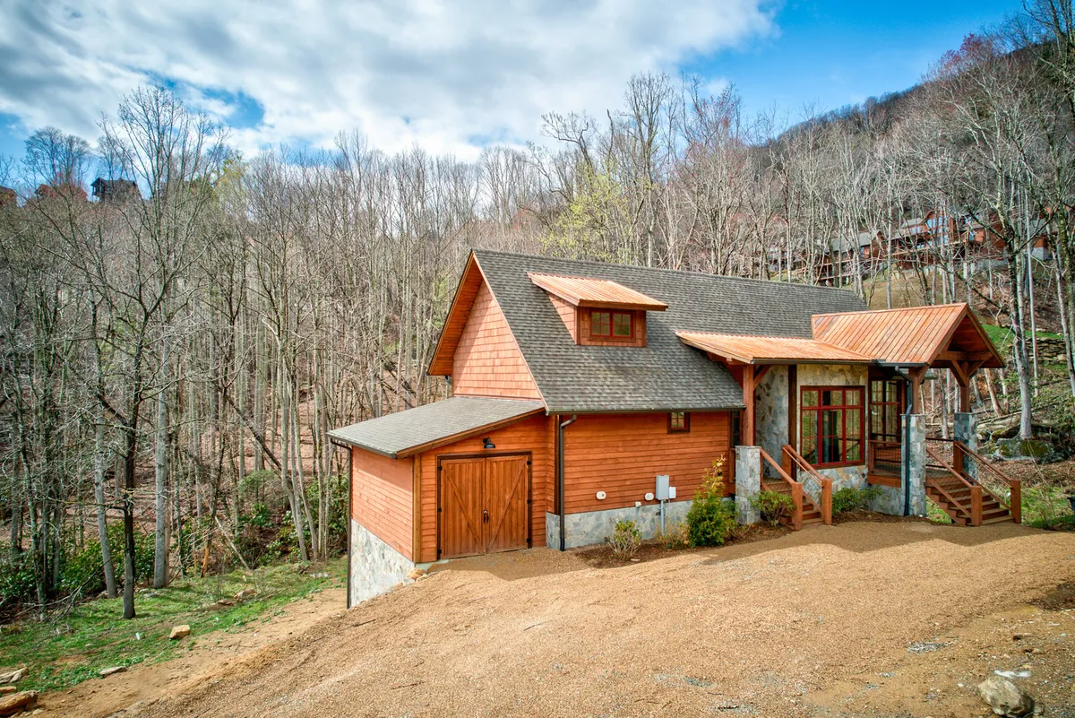 This exterior image features Vesper Lodge's inviting wooden structure with stone foundation, large windows, and copper roof accents, all set amidst a serene mountain environment. The spacious porch and natural surroundings are visible, evoking the sense of a mountain retreat ideal for outdoor relaxation and family gatherings.