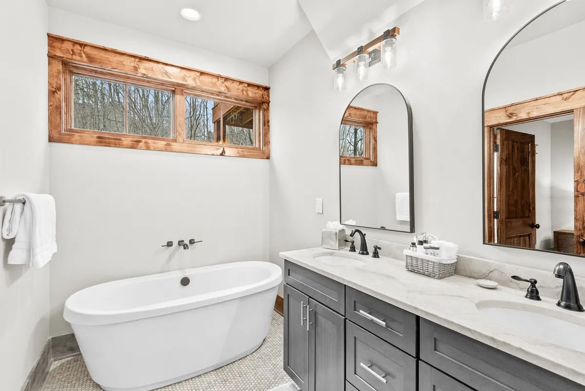An elegant bathroom with a freestanding soaking tub, double granite vanity, large mirrors, and wood-framed windows. The space feels tranquil and indulgent, ideal for relaxation after adventurous days.