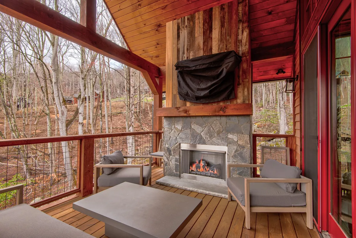 A comfortable outdoor lounge area centered around a stone fireplace, with plush seating under sturdy wooden beams and surrounded by trees. The space is designed for relaxation, socializing, and soaking in mountain sunsets or starry nights.