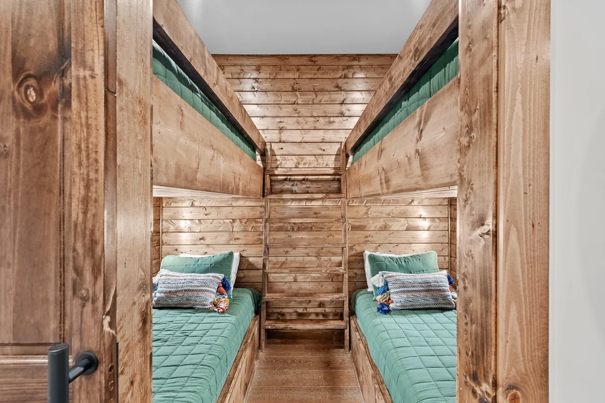 A playful bunk nook with twin-over-twin built-in beds, surrounded by wooden walls and adorned with colorful pillows. The cozy space is inviting and fun, perfect for children or those young at heart.