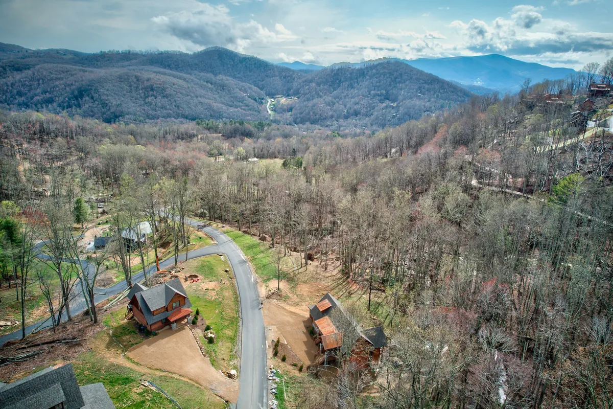 A sweeping view of the surrounding mountain landscape, showcasing rolling hills, scattered cabins, winding roads, and abundant trees. The image captures the broader Eagles Nest community and the scenic beauty that guests can explore during their stay.