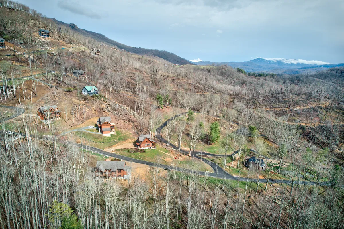 A serene exterior view of the Eagles Nest community, featuring rolling mountains, scattered wooden cabins, and a winding road. The scene is peaceful and highlights the beautiful natural surroundings available for exploration and outdoor activities.