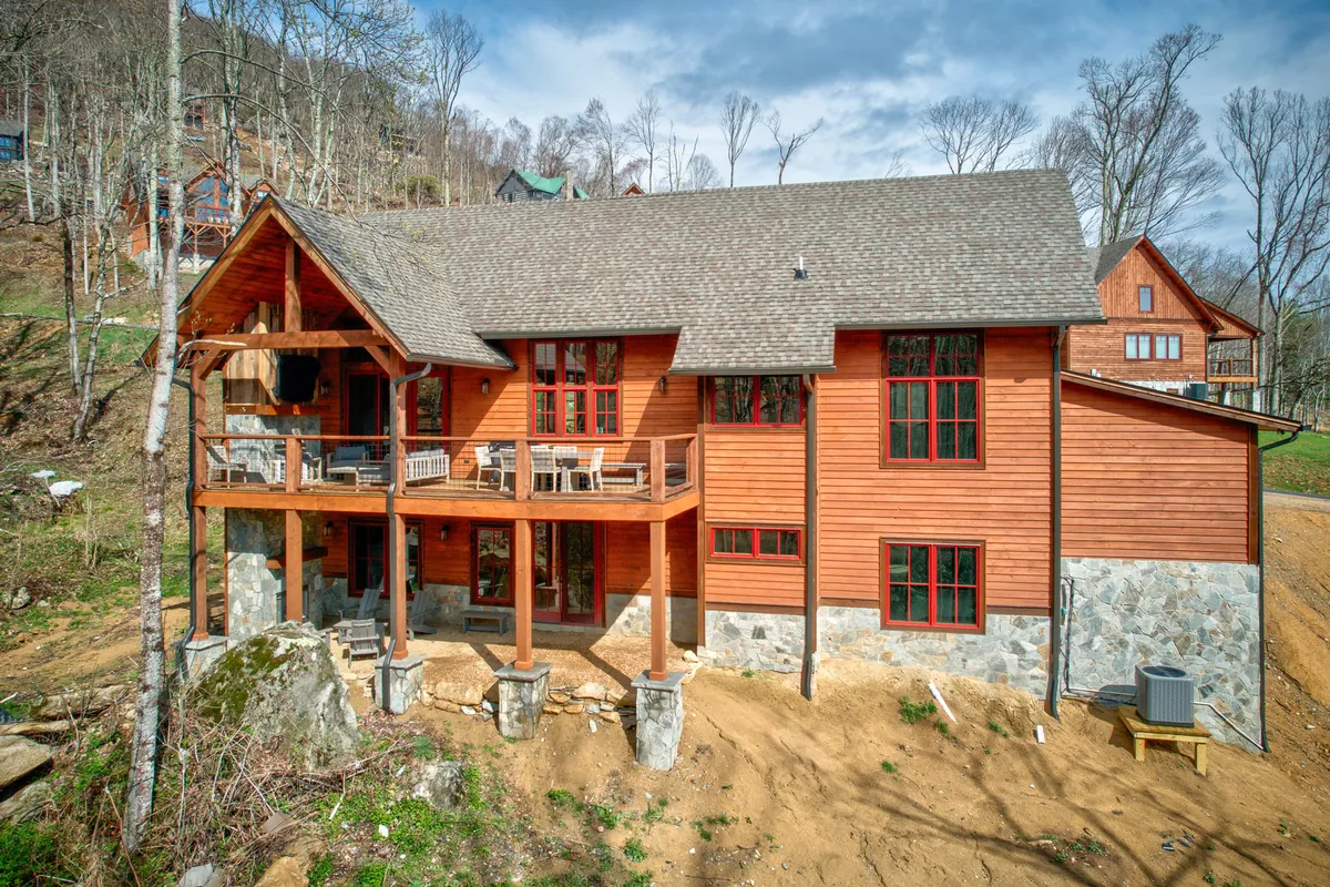 A cozy wooden deck with chairs, large windows, and a stone foundation nestled among trees. The setting is ideal for family gatherings, outdoor barbecues, and relaxation in a natural mountain environment.